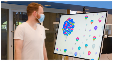 A person walks by a large screen display showing SkyGlyphs, a data visualization that we designed to have a nonconventional data representation to captivate people’s attention and leverage their curiosity to explore a dataset.